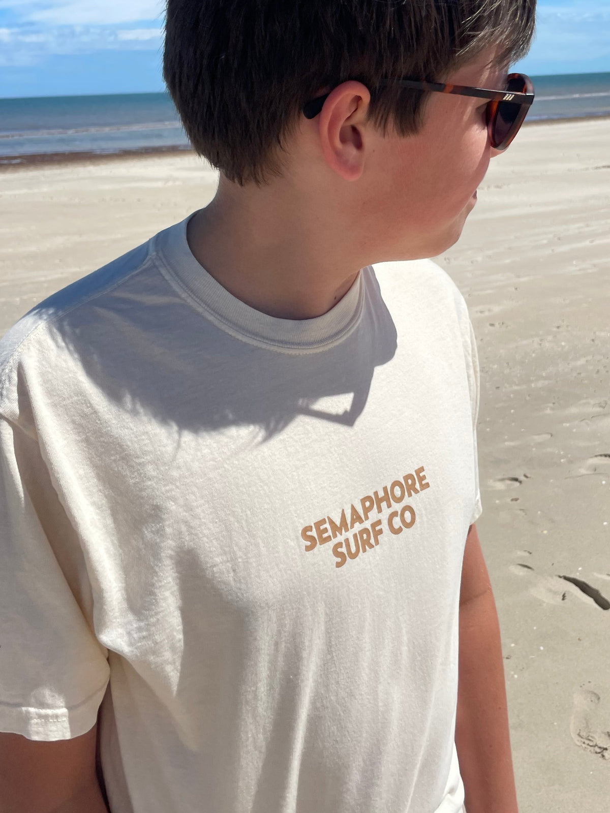 Person wearing the natural Semaphore Surf Co. emblem tee on the beach