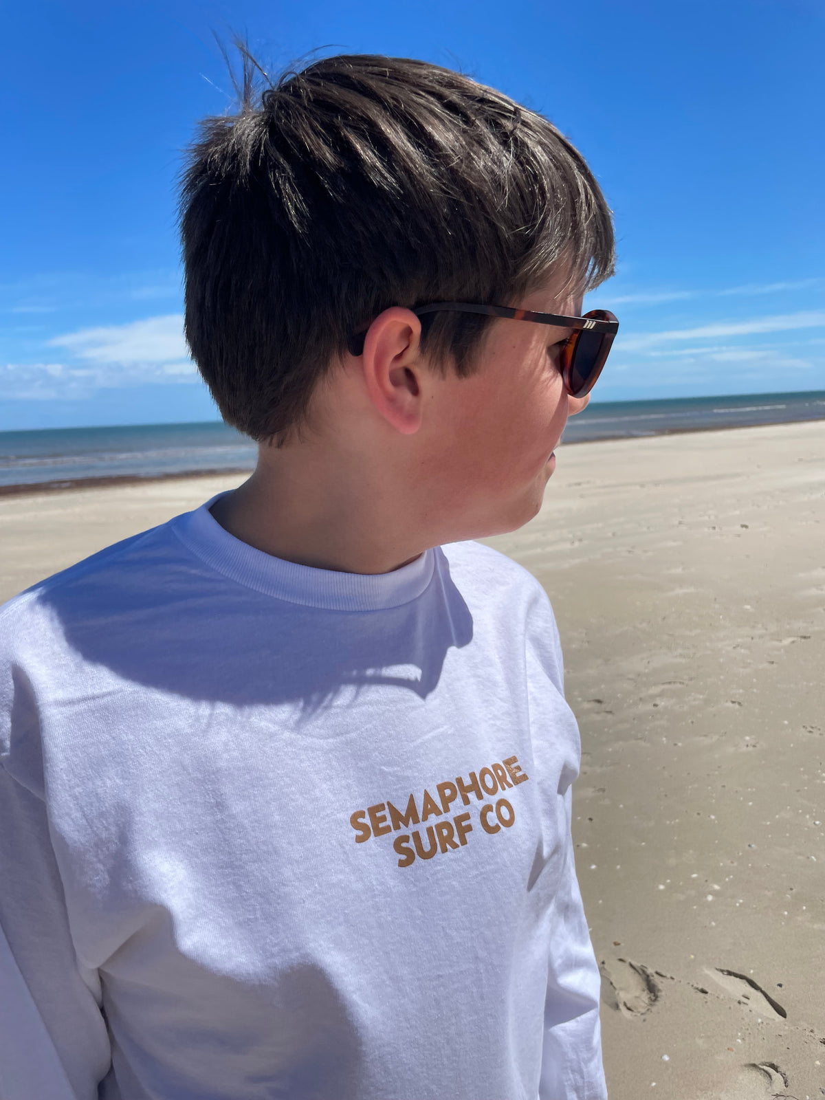 Person wearing the white Semaphore Surf Co. long sleeve tee on the beach, front view