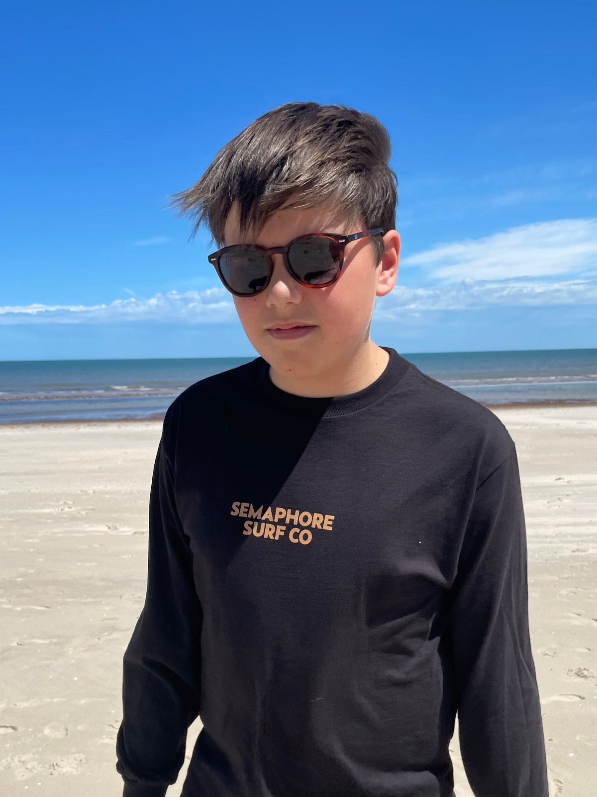Person wearing the black Semaphore Surf Co. long sleeve tee on the beach, front view
