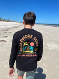 Person on the beach wearing the black long sleeve tee, back view showing the full-colour emblem
