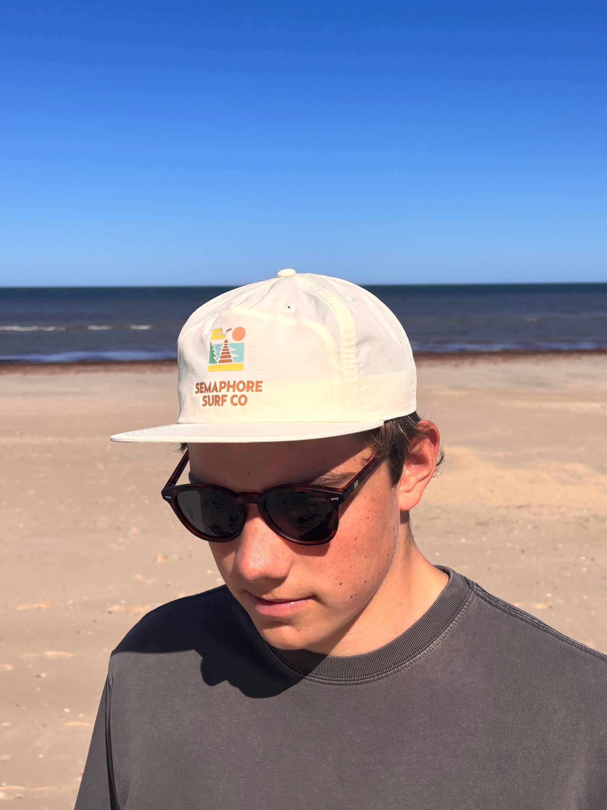 Person wearing the natural Semaphore Surf Co. surf cap and sunglasses on the beach