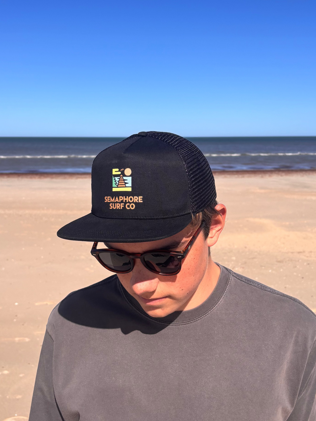 Black mesh-back trucker cap with the colour Semaphore Surf Co. jetty icon and wordmark on the front