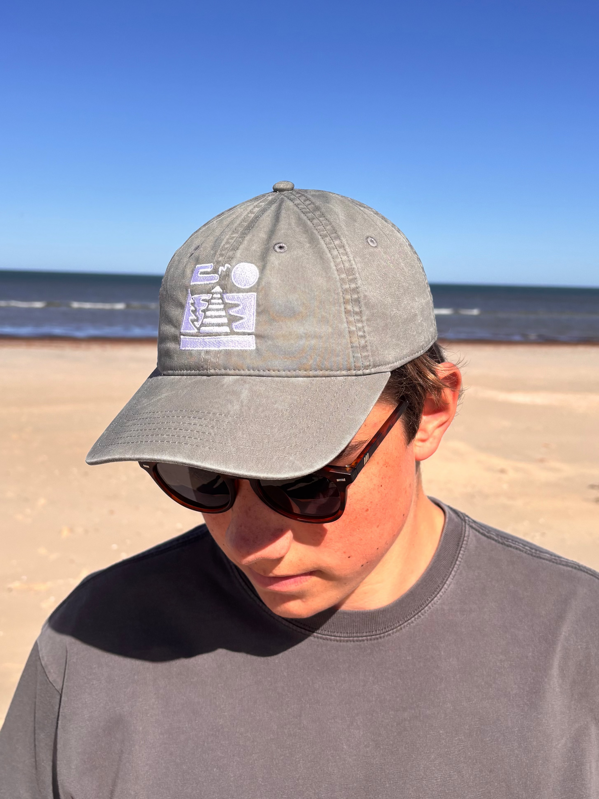 Person wearing the faded charcoal Semaphore Surf Co. cap on the beach