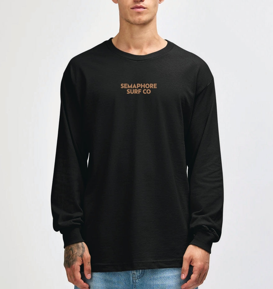 Model wearing the black Semaphore Surf Co. emblem long sleeve tee, front view with the wordmark on the chest