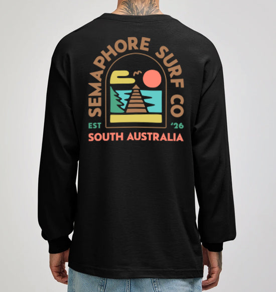 Model wearing the black Semaphore Surf Co. emblem long sleeve tee, front view with the wordmark on the chest